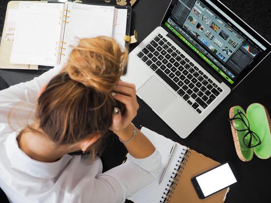 riesgos biopsicosocial mujer rubia con rodete sostiene su cabeza con ambas manos frente a computadora portatil sobre escritorio en señal de estrés